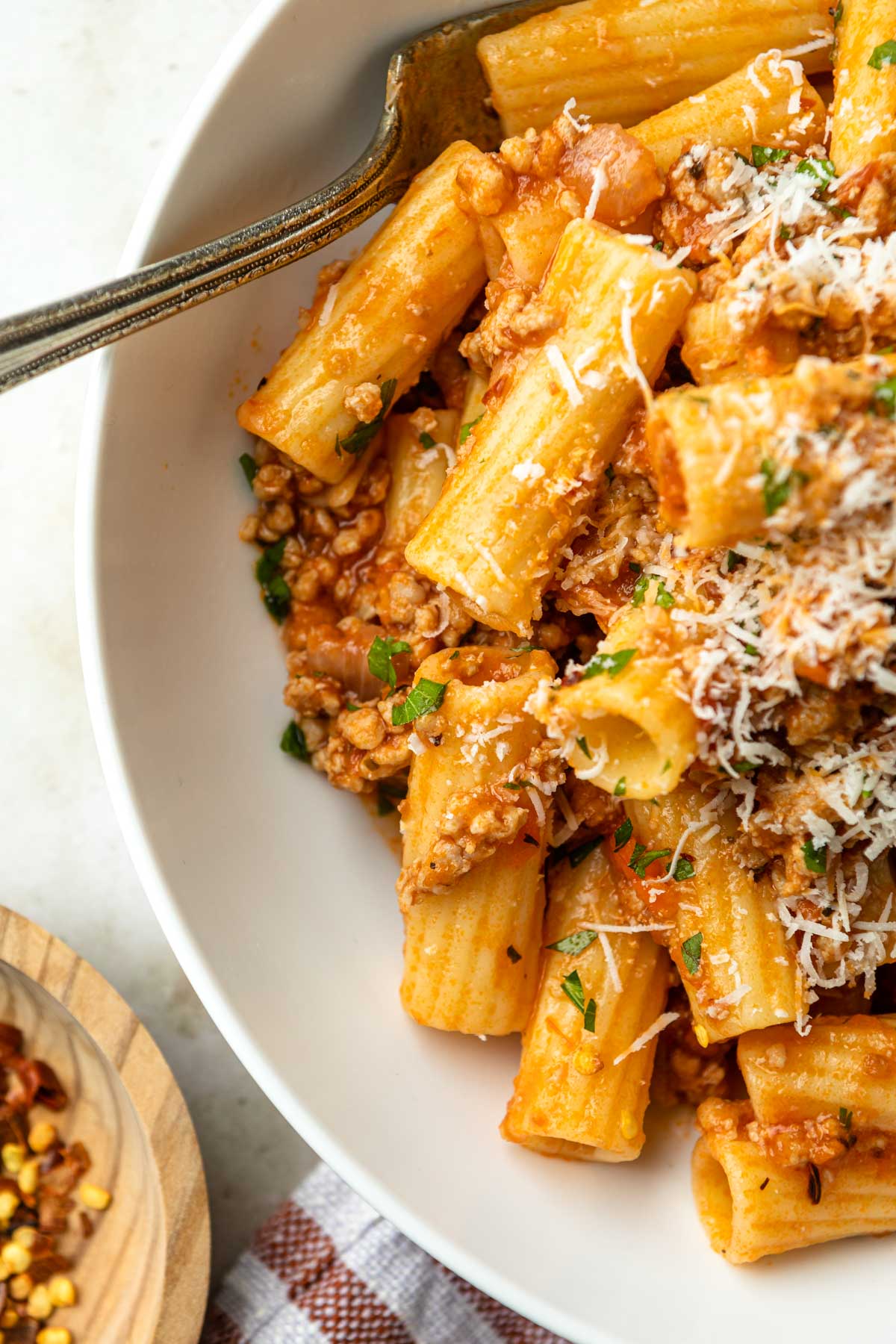 Close up of a bowl of rigatoni with pork ragu, garnished with grated pecorino romano cheese and fresh chopped parsley. 