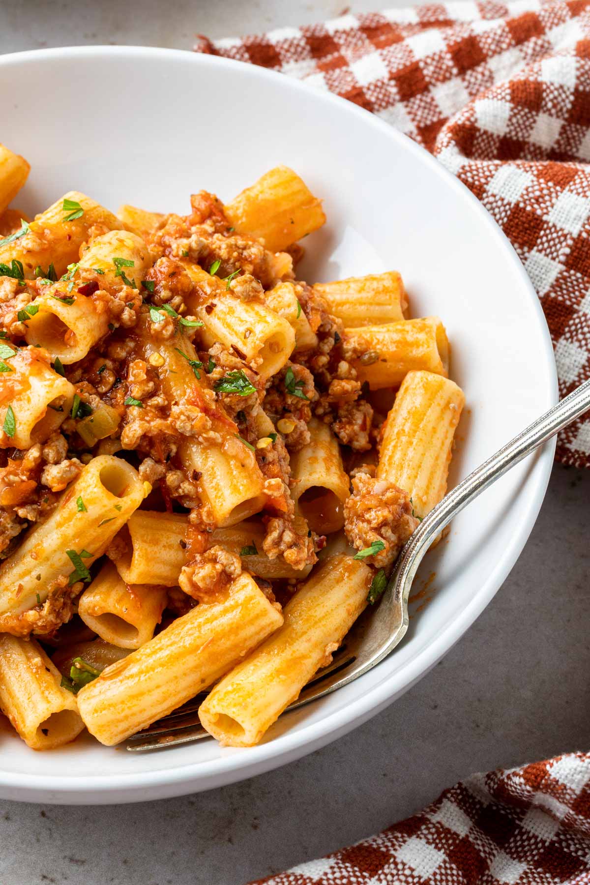A close up of a bowl of rigatoni with pork ragu with a fork in the bowl. 